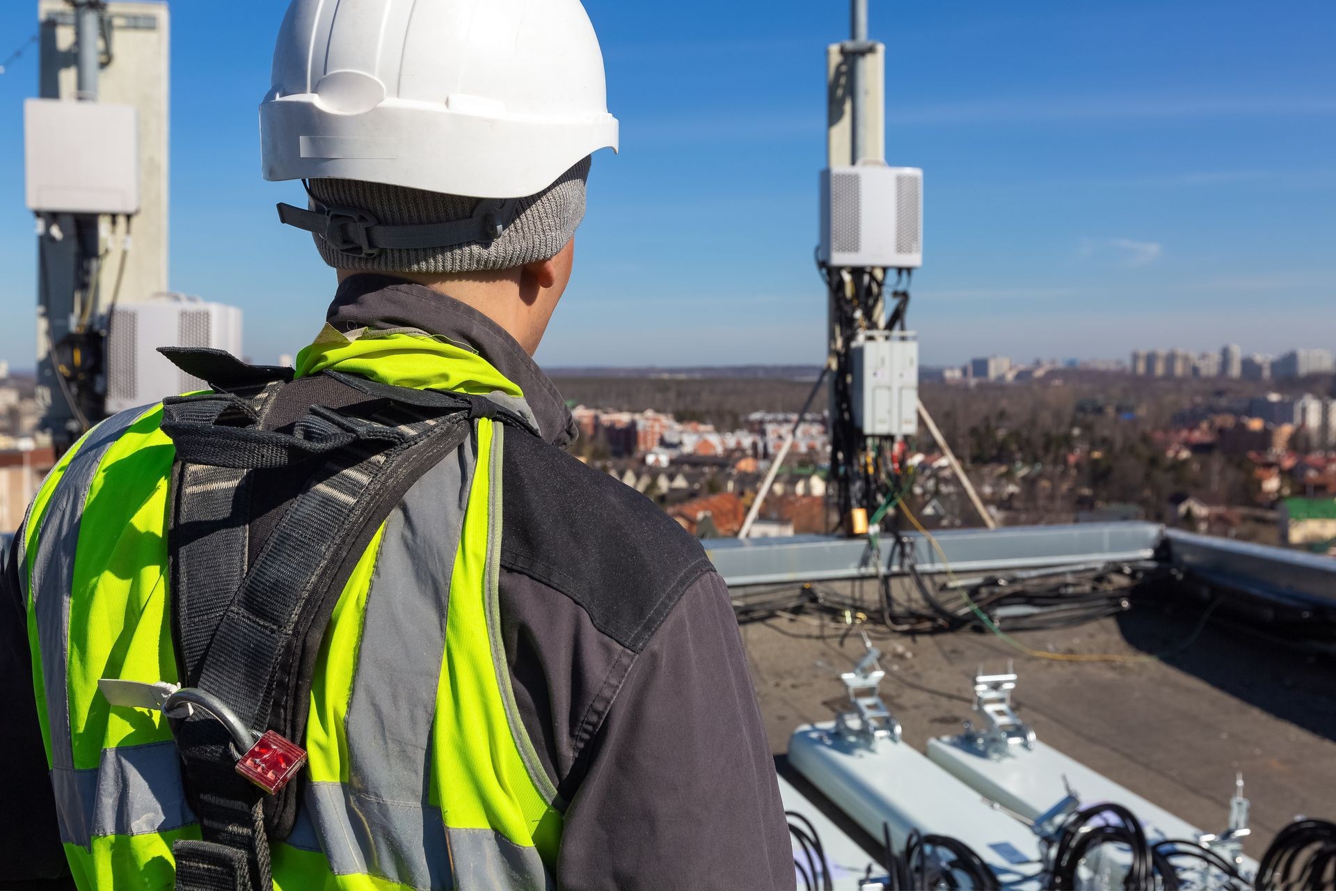 Professional industrial climber in helmet and uniform  and  antennas of GSM  DCS UMTS LTE bands, outdoor radio units  on the roof. Working process of upgrading telecommunication equipment.